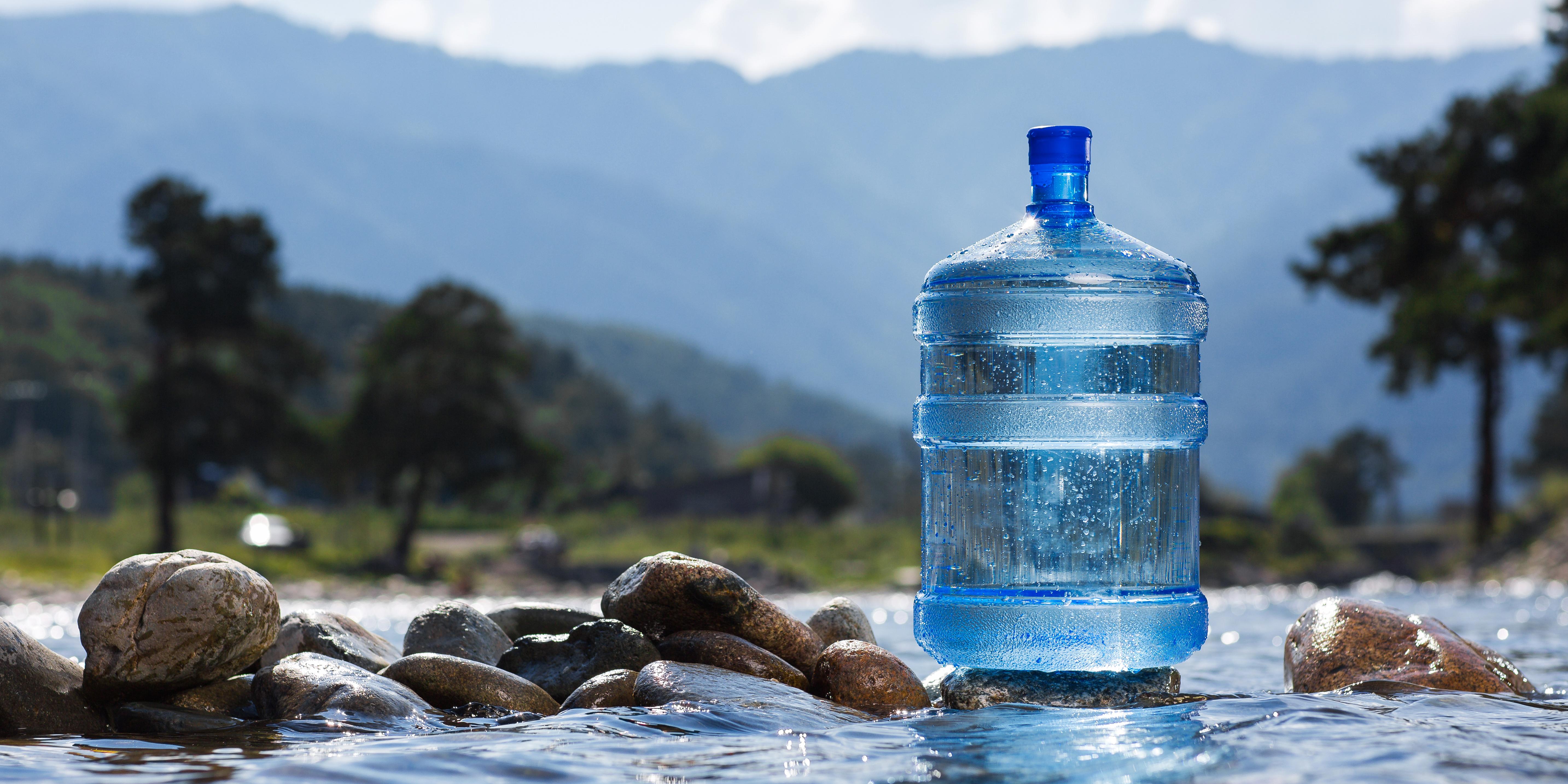 a blue plastic jug of bottled water floating on rocks in a natural stream