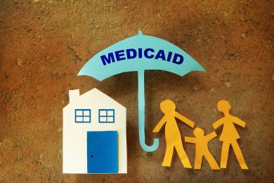 Paper cutouts depicting a house, a family, and a Medicaid umbrella protecting them