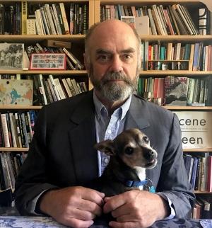 Photo of Winet holding small dog, shelves of books behind him
