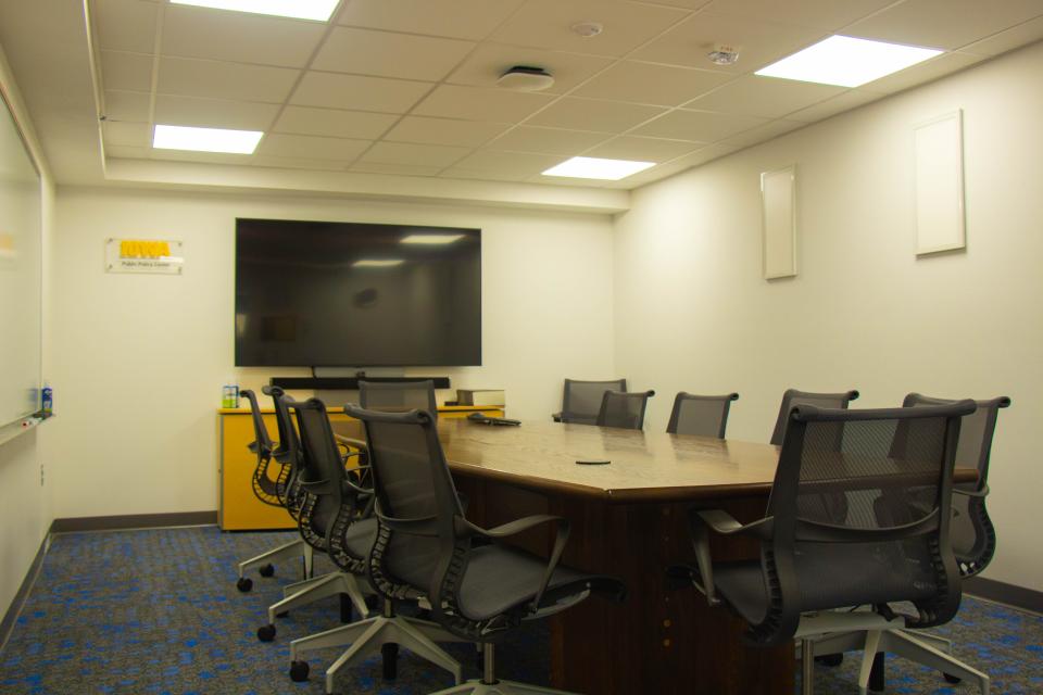 a conference room with a large table and chairs around it, a large tv, and a plaque in the corner of the wall reading "Public Policy Center"