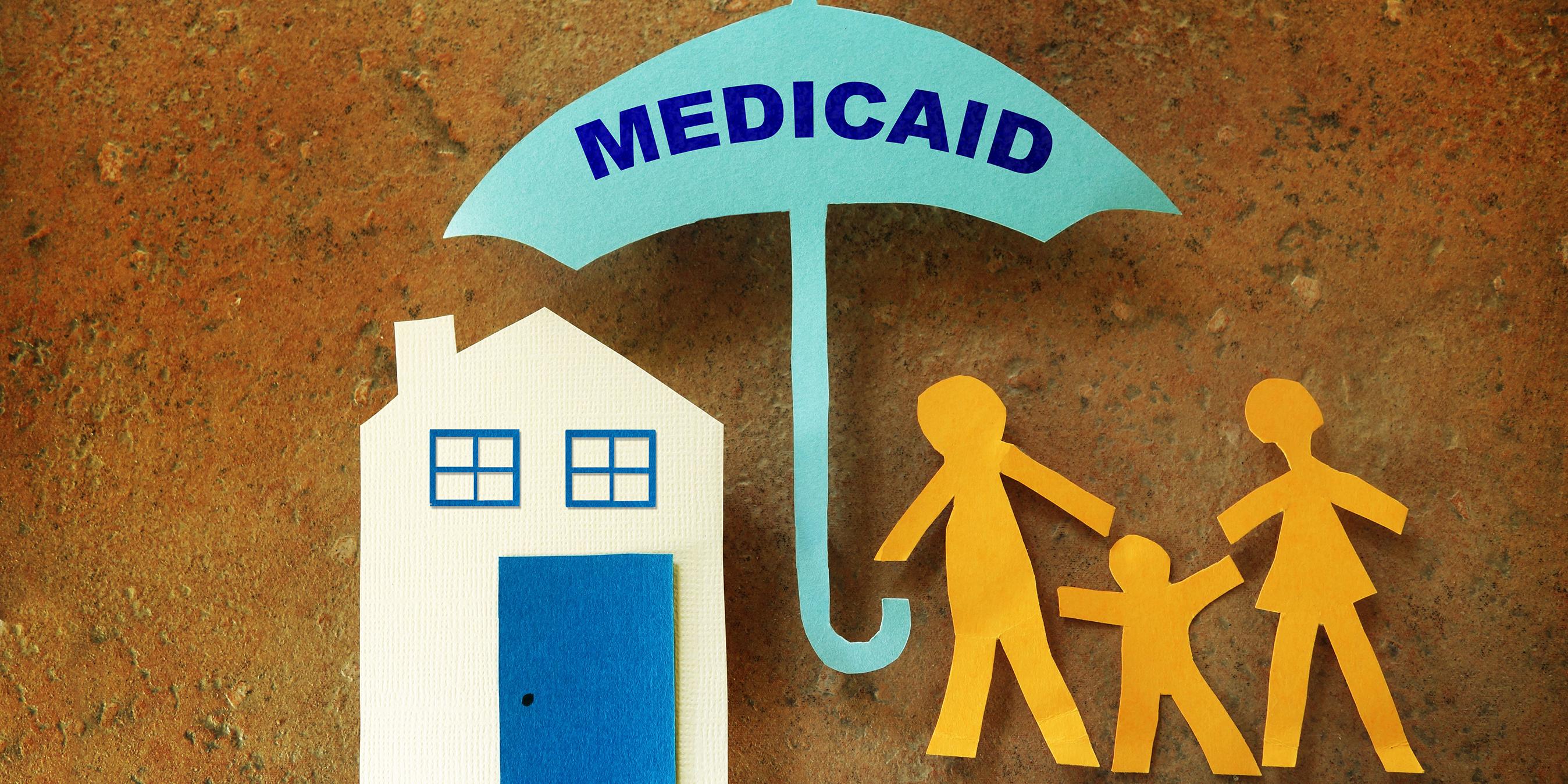 Paper cutouts depicting a house, a family, and a Medicaid umbrella protecting them