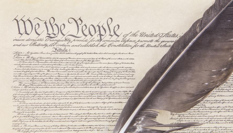 Sketch of the US Constitution's preamble and first article, with a feather quill laying over the document