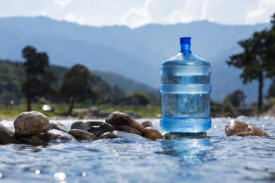a blue plastic jug of bottled water floating on rocks in a natural stream