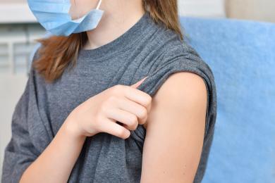 masked adolescent with sleeve pulled up for vaccination