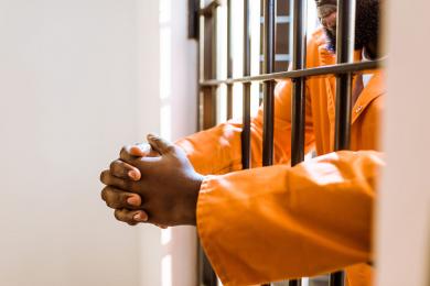 A man stands with his arms through prison bars