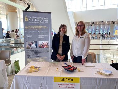 Lisa Halm-Werner and Cassidy Branch pose at the PPC/ISRC table at the Research Services Fair. There is candy on the table and a poster displaying information about PPC/ISRC to the right of Lisa.
